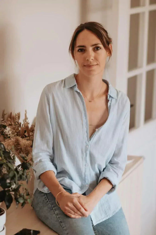 Alice Monney, Health professional collaborating with SOVA, wearing a light blue striped shirt, sitting indoors in a calm and natural setting.