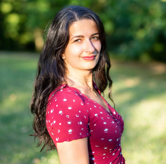 Jade Dulieu, Health professional working with SOVA, smiling outdoors in a red floral dress, with greenery in the background.