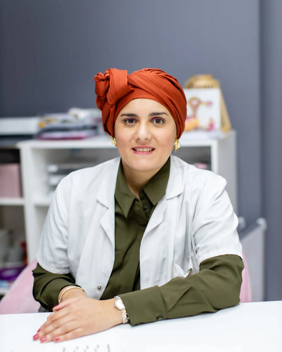 Dr Rabab MOSBAH, Health professional wearing a white coat and orange headscarf, smiling at a desk.